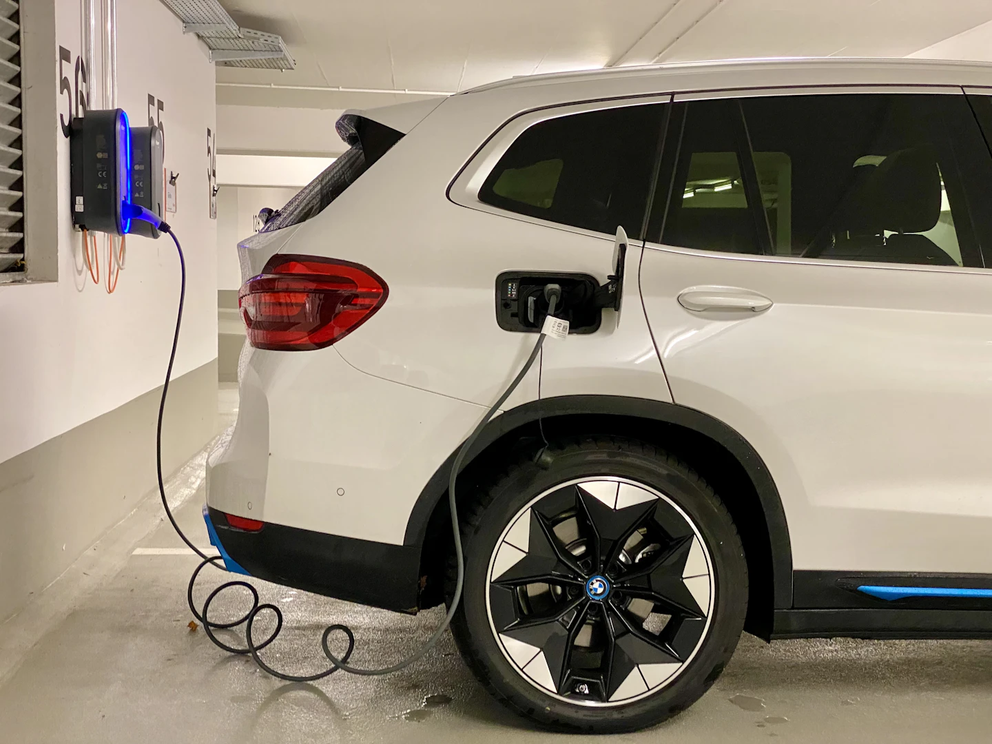 White electric SUV plugged into a wall-mounted charger in a parking garage